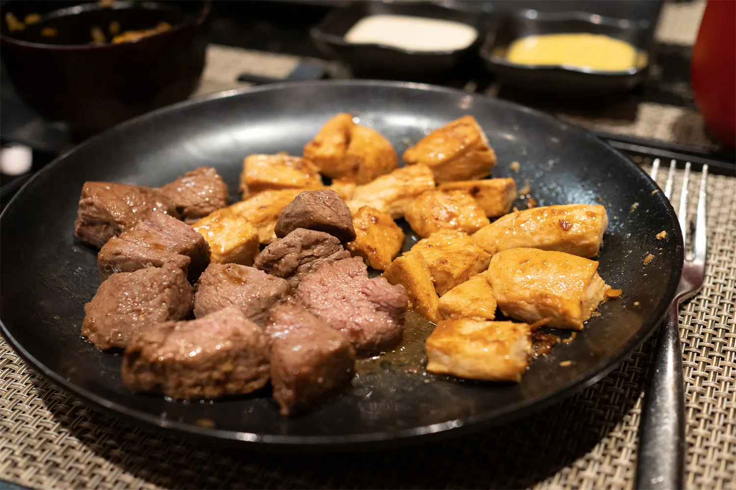 Seared beef and chicken cubes on a black plate