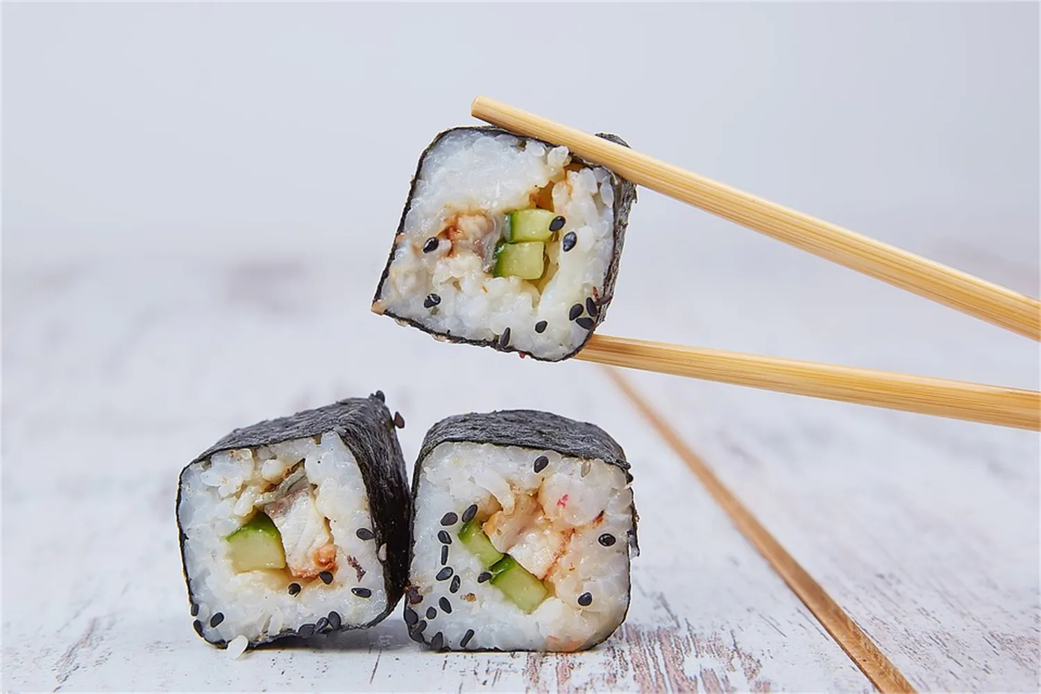 Shrimp cucumber maki roll held by wooden chopsticks